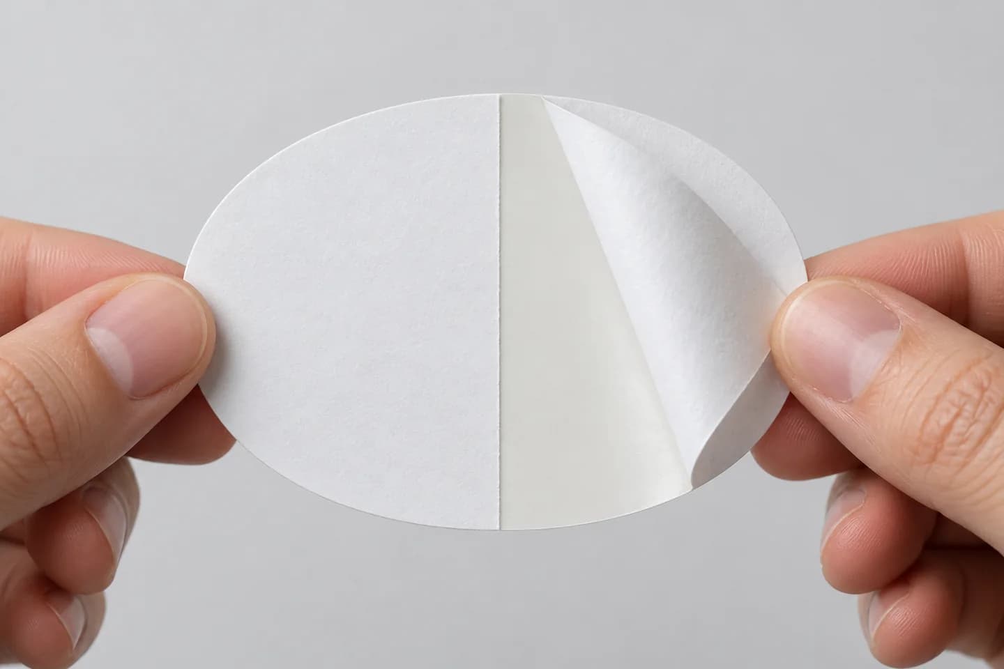 Illustration of hands peeling an oval sticker's backing from its center split